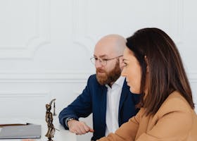 Man and woman discussing legal documents indoors, featuring Lady Justice statue.